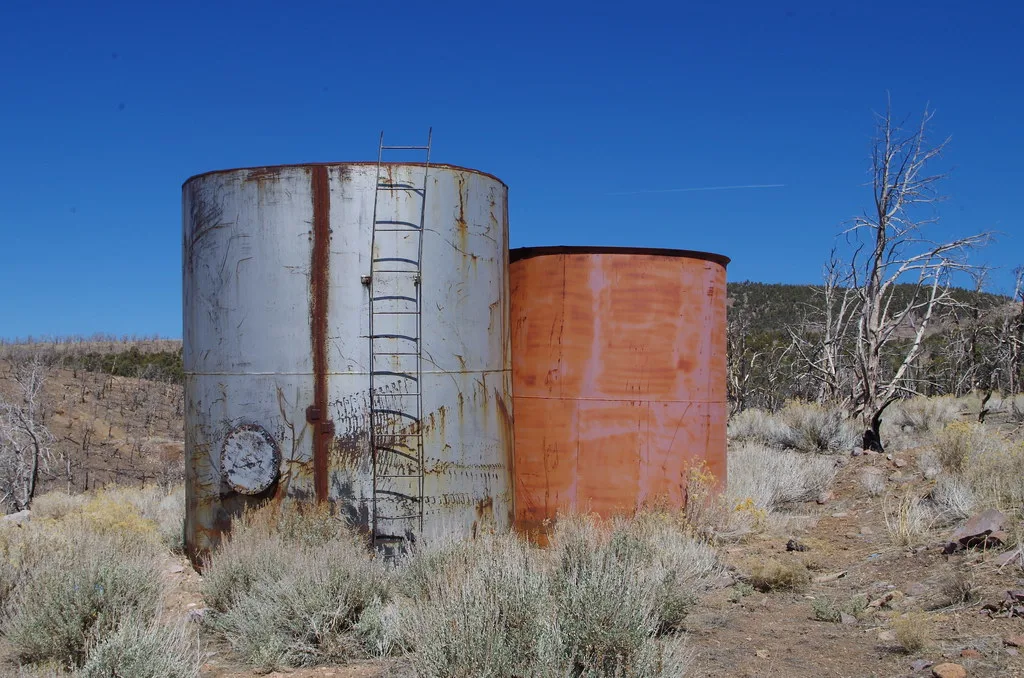 Two old rusty metal tanks on dry ground.