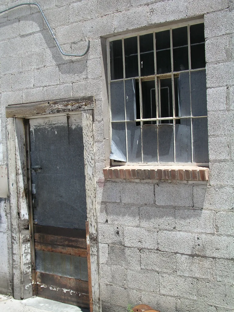 Decaying door and broken window in a concrete block wall.
