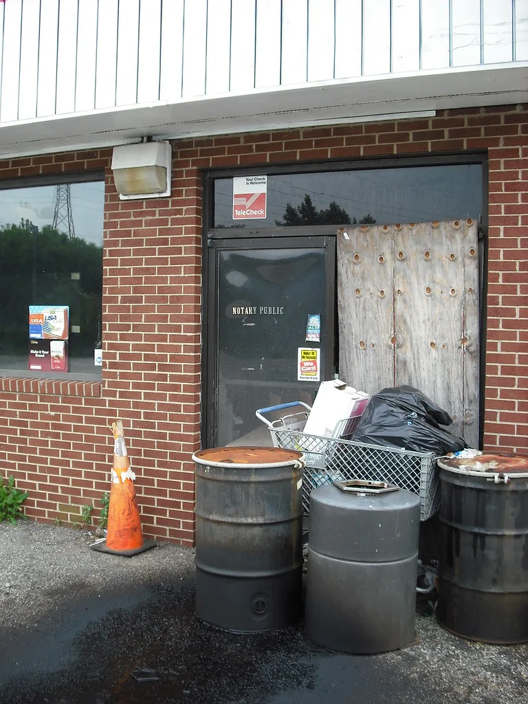 Boarded entrance of an old building obstructed by drums and waste.