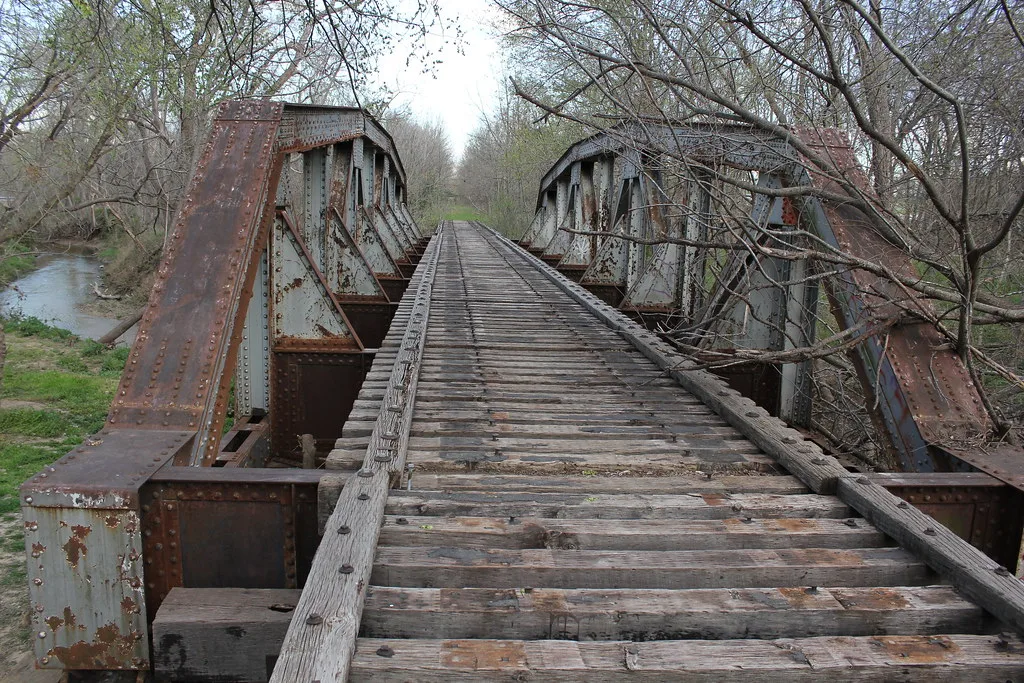 Pont ferroviaire désaffecté aux poutres rivetées rouillées au-dessus d’un cours d’eau.