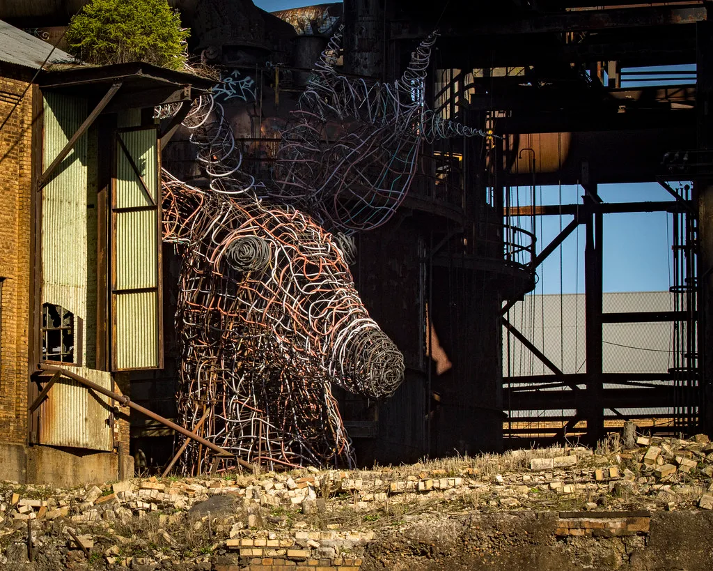 Structure industrielle ruinée avec sculpture de tête animale en métal.