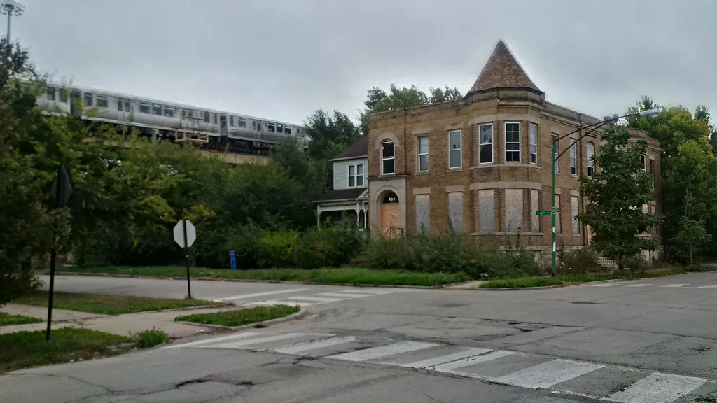 Old corner building with a turret and boarded windows near a railway line.