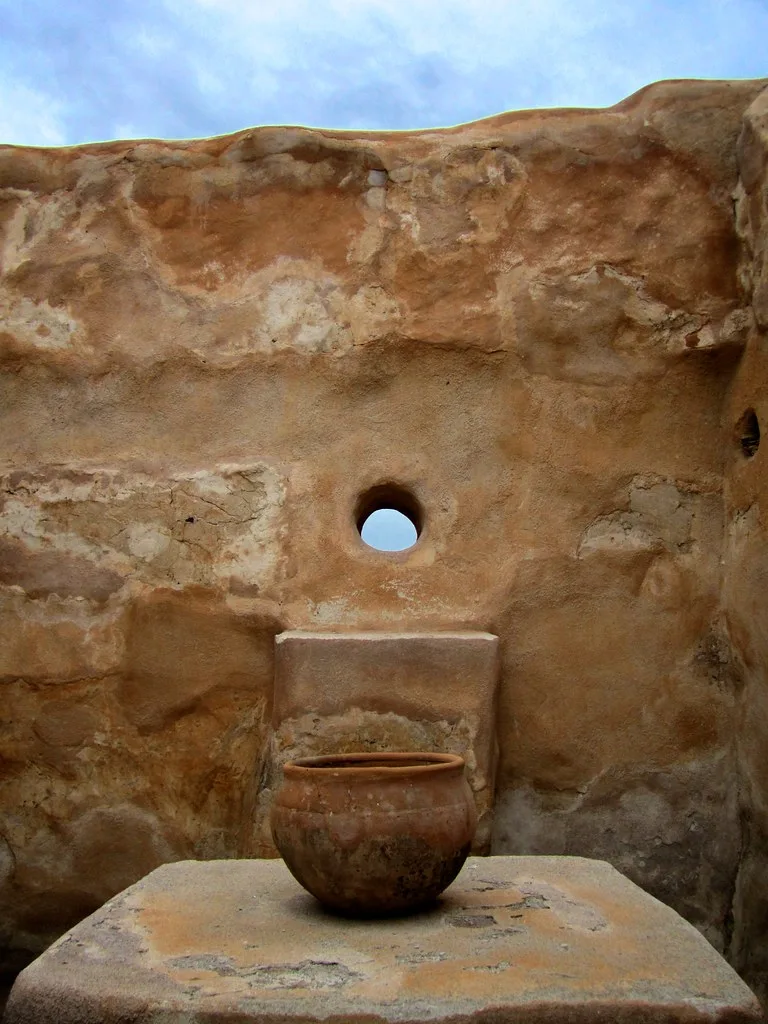 Mur ancien à ouverture ronde avec un récipient posé sur un socle maçonné.