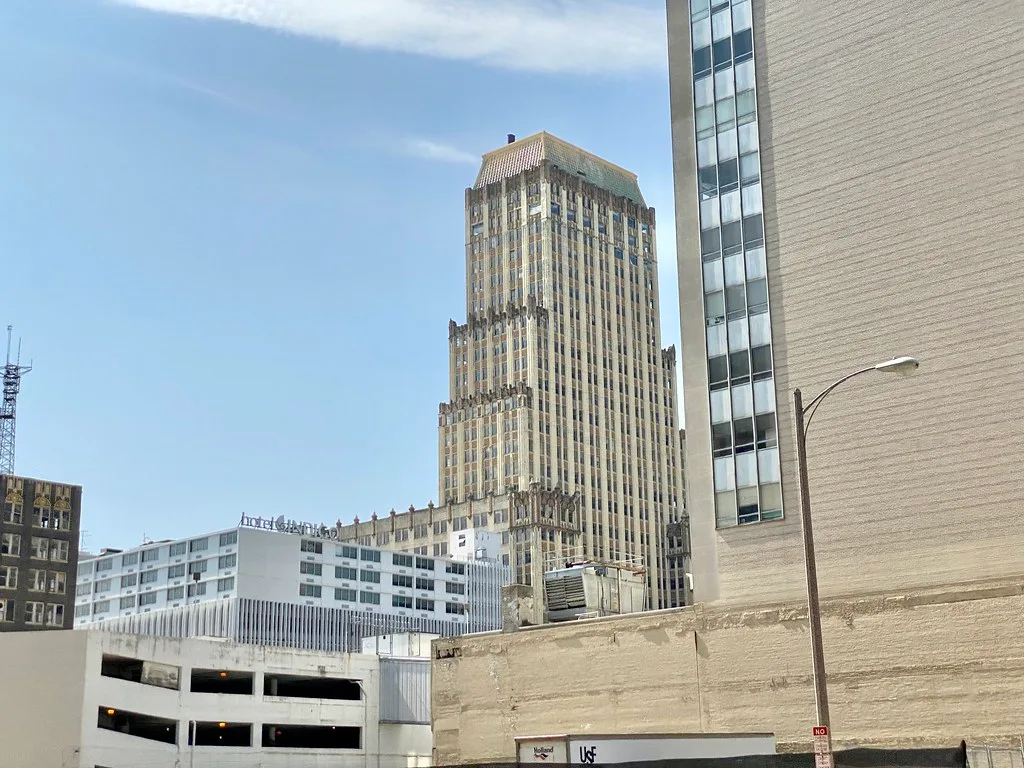 Old tower with an ornate weathered facade among city buildings.
