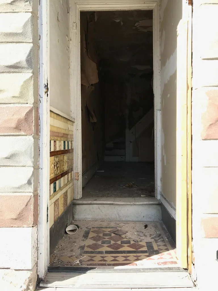 Entrée carrelée donnant sur un escalier et des murs dégradés.