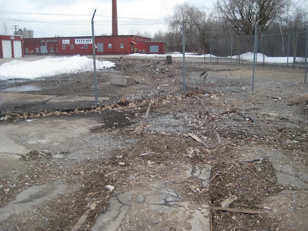 Bent rails and debris in a deteriorated industrial surface behind a fence.