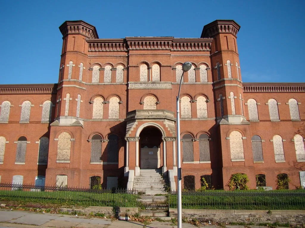 Large red brick building with sealed windows and plants growing through its entrance steps.