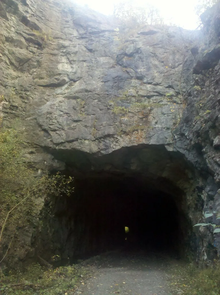 Intérieur d’un ancien tunnel rocheux au sol de gravats, ouvert à son extrémité.