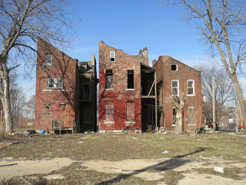 Abandoned red-brick houses with gutted upper floors and boarded or empty windows beside bare trees.