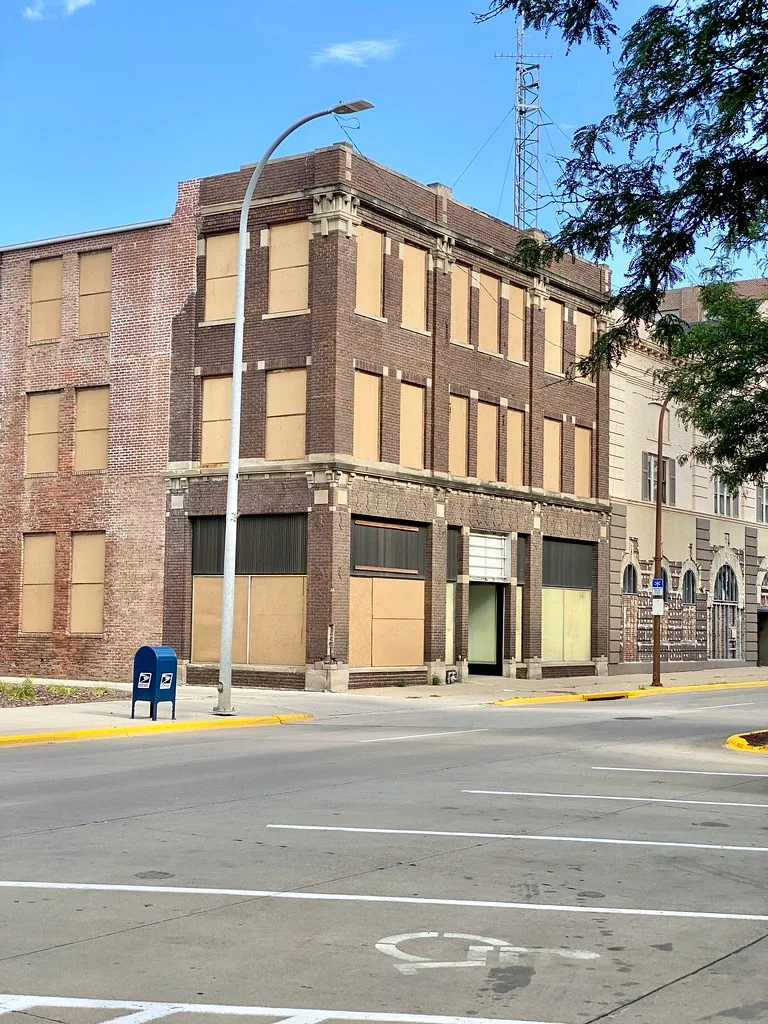 Three-story brick commercial building with windows and storefronts sealed with beige boards.