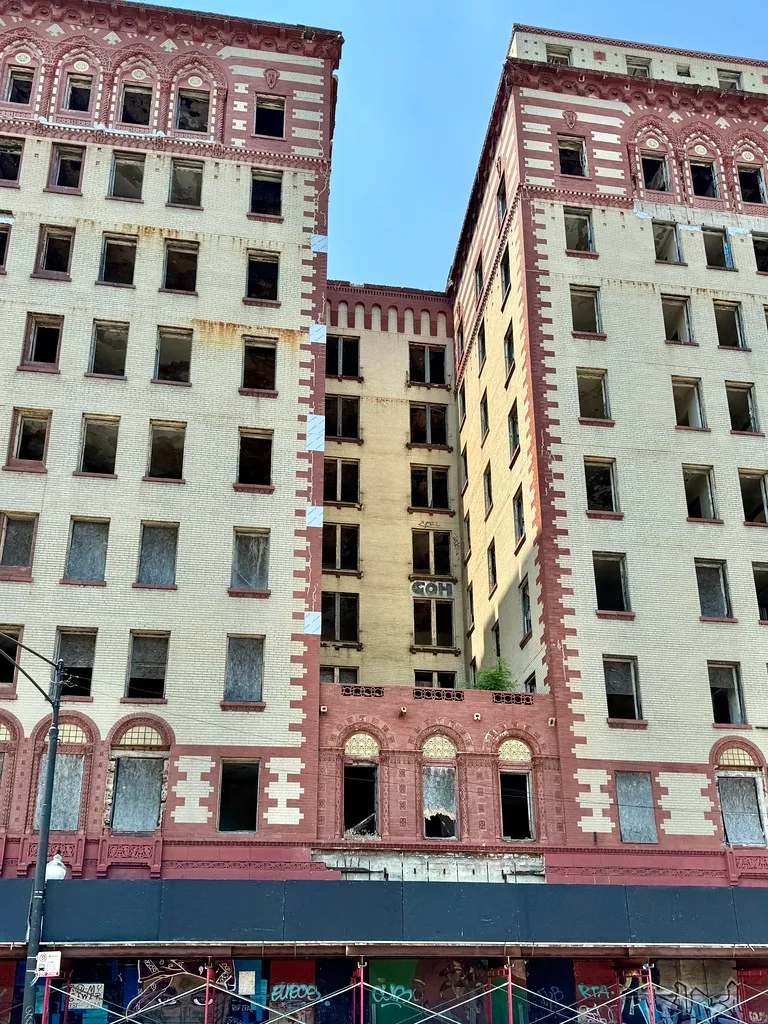 Large abandoned building with cream and red facades pierced by many broken windows.