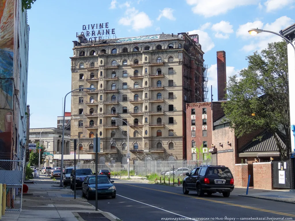 Ancien Divine Lorraine Hotel aux nombreuses fenêtres vides derrière une clôture urbaine.