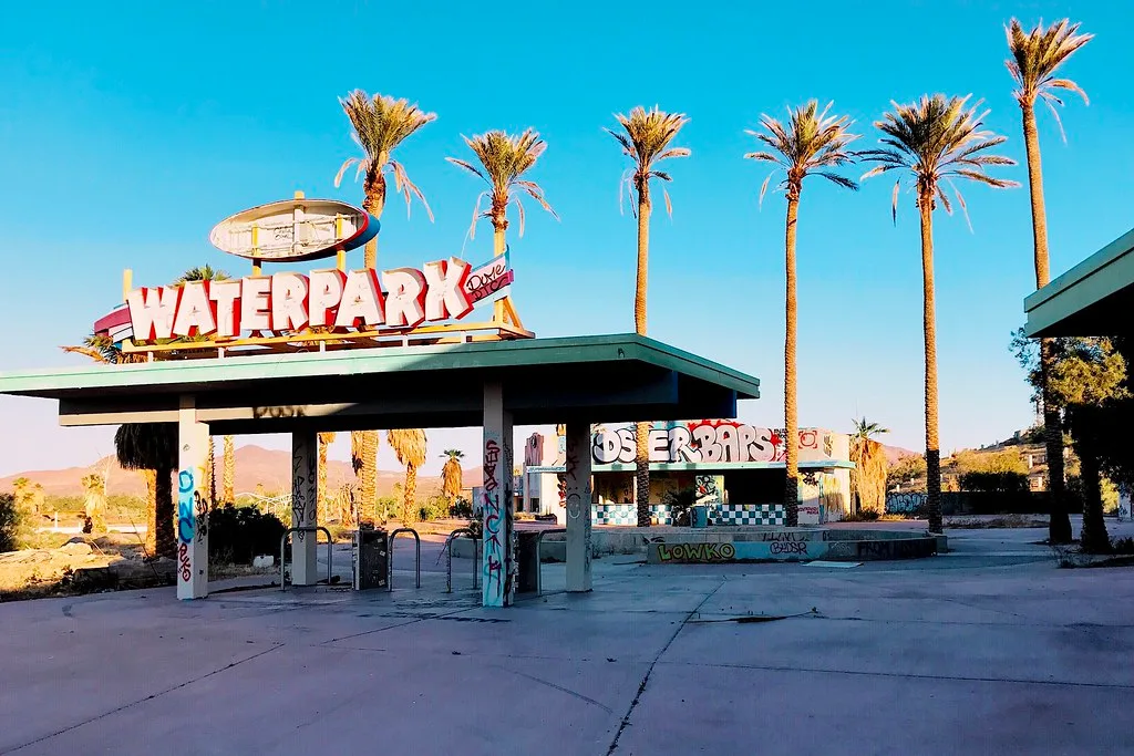 Graffiti-covered entrance to a former water park with a sign and palm trees.