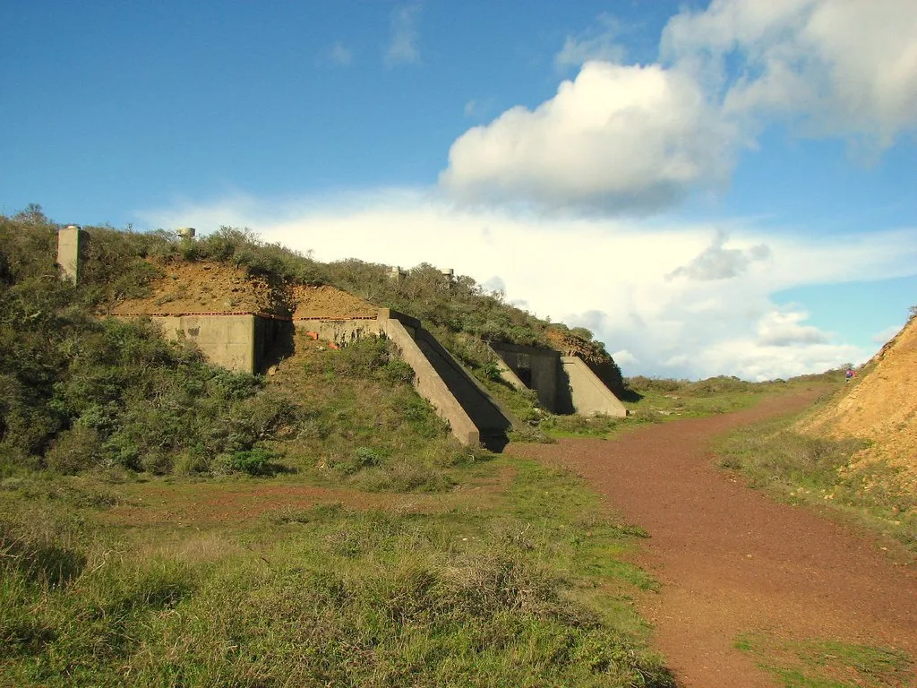 Remains of partly buried concrete structures with sloping walls beside a dirt path.