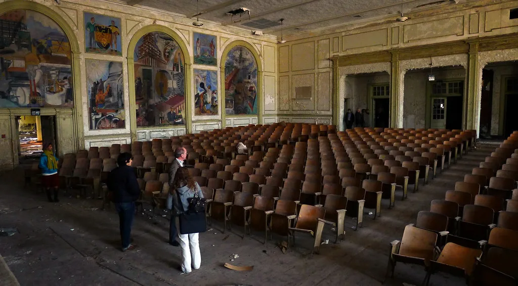 Ancienne salle de spectacle délabrée aux rangées de fauteuils bruns.