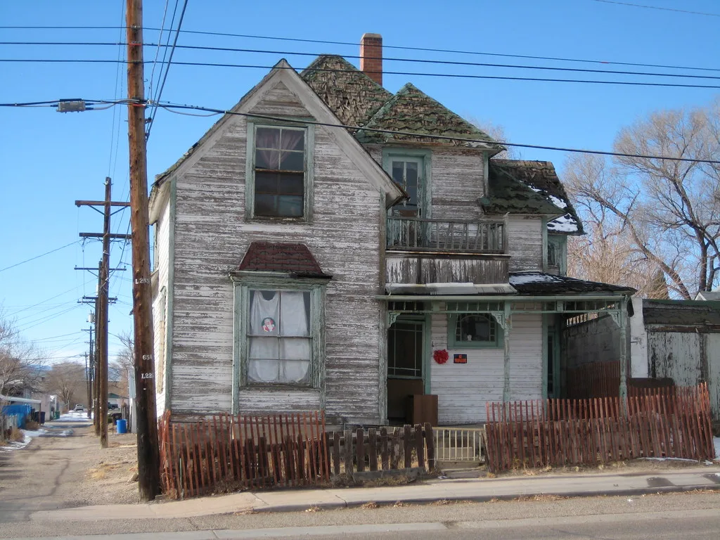 Ancienne maison blanche à la toiture et au bardage très dégradés.