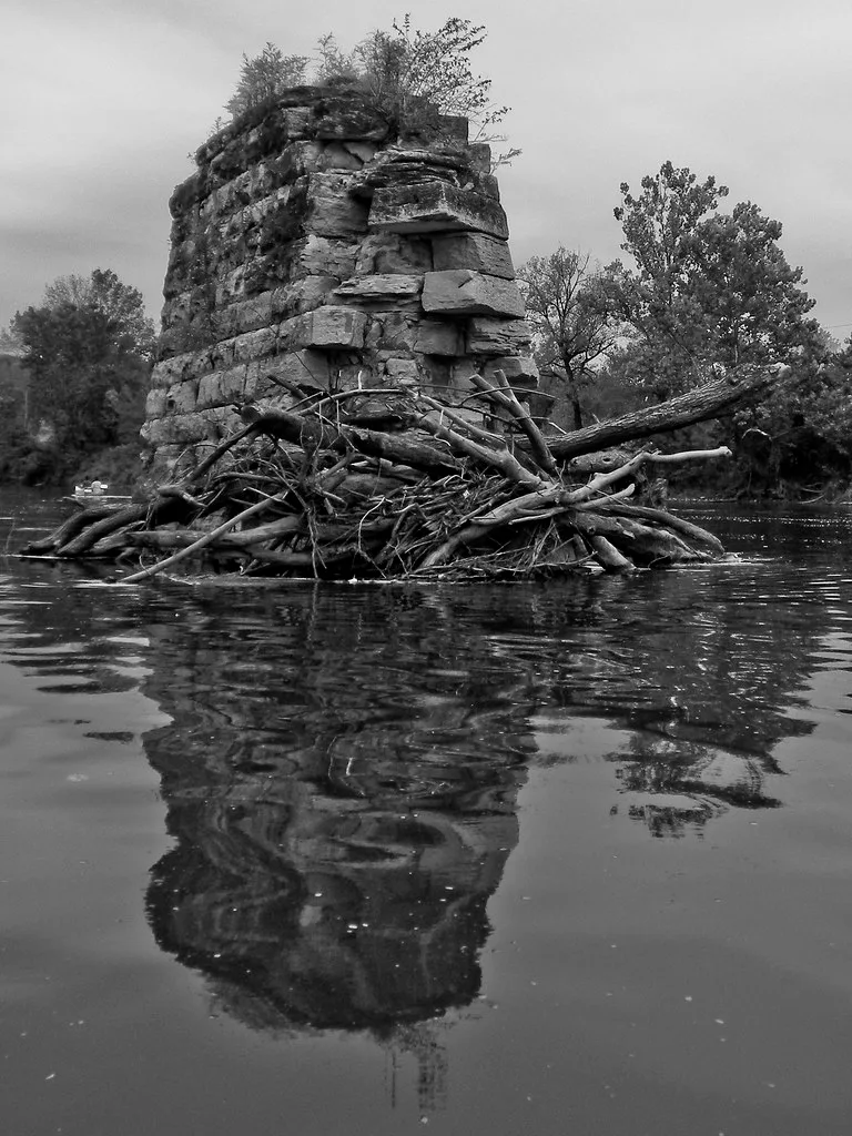 Old stone bridge pier surrounded by branches in a river.