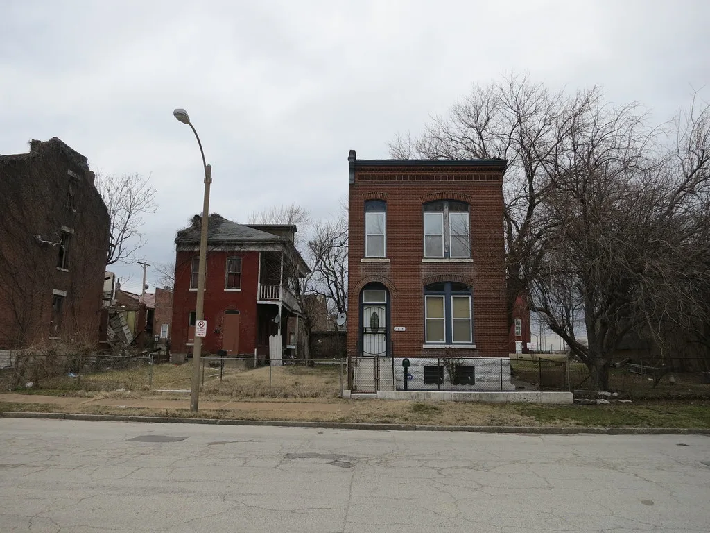 Maisons dégradées à côté d’une maison en briques entretenue.