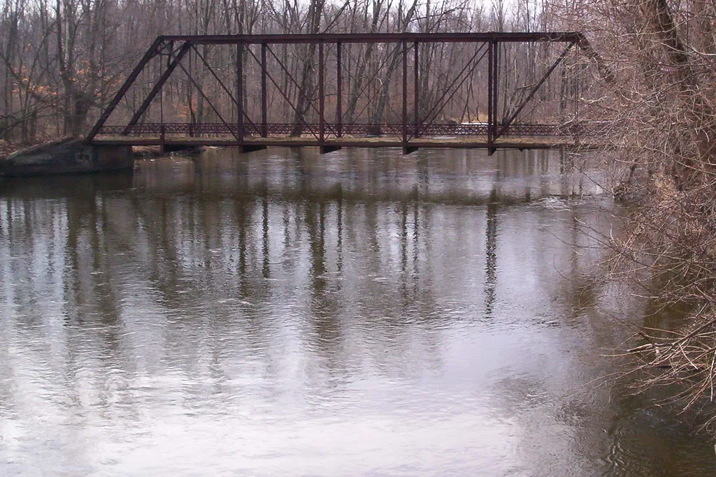 Old metal truss bridge over a wooded river.