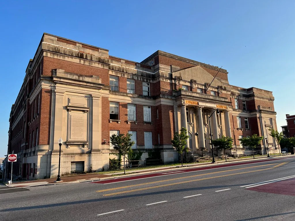 Monumental red brick building with pale columns and numerous sealed windows.