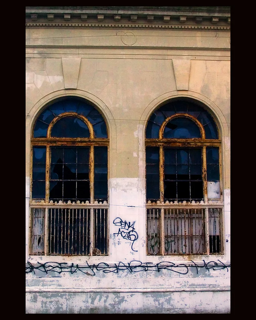 Deux fenêtres cintrées brisées dans une façade couverte de graffitis.