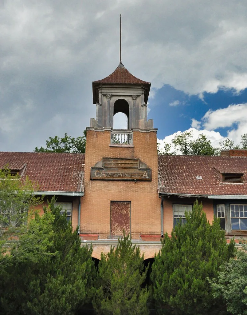 Old brick hotel with a small bell tower above bushes.