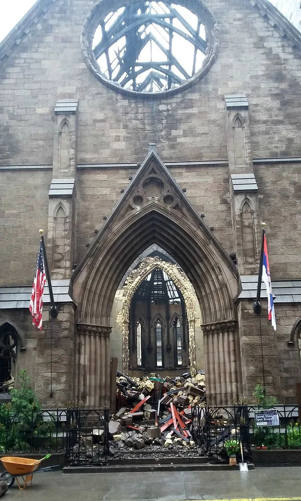 Portail d’une église ruinée avec gravats et charpente à ciel ouvert.