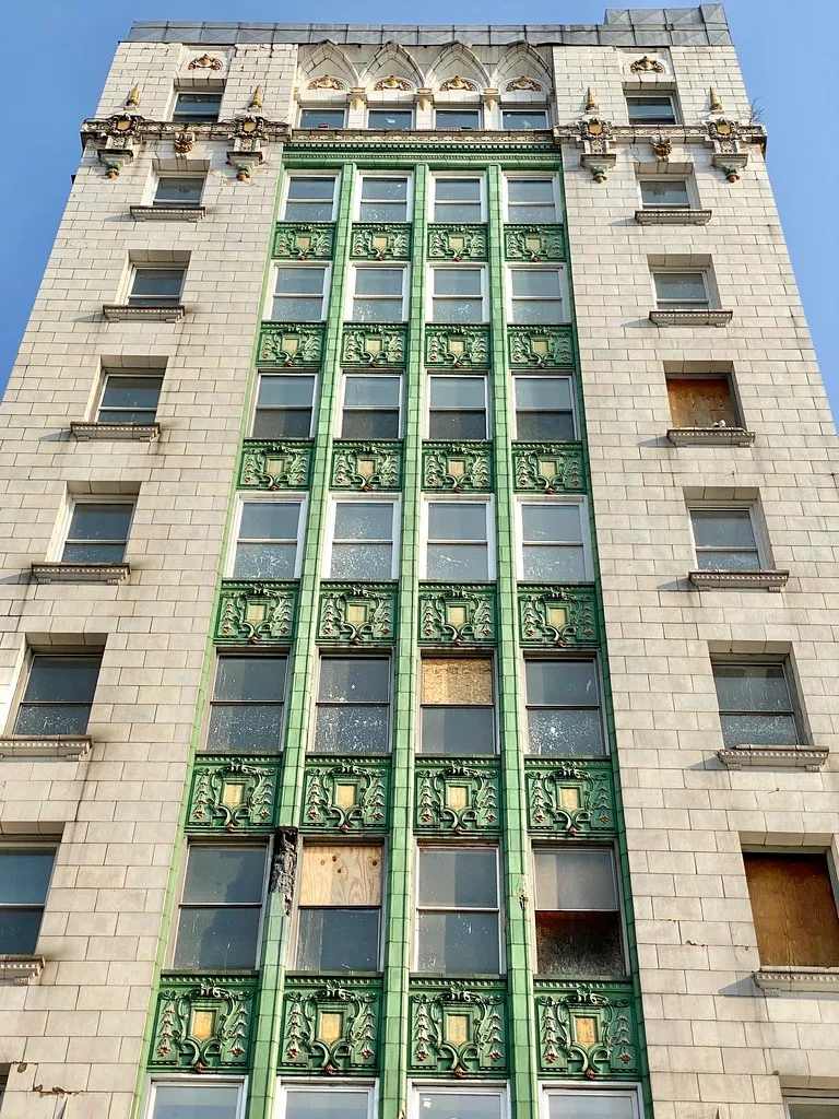 Green ceramic ornament on a neglected building facade with broken or boarded windows.